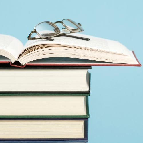 stack of books, with top one open and glasses